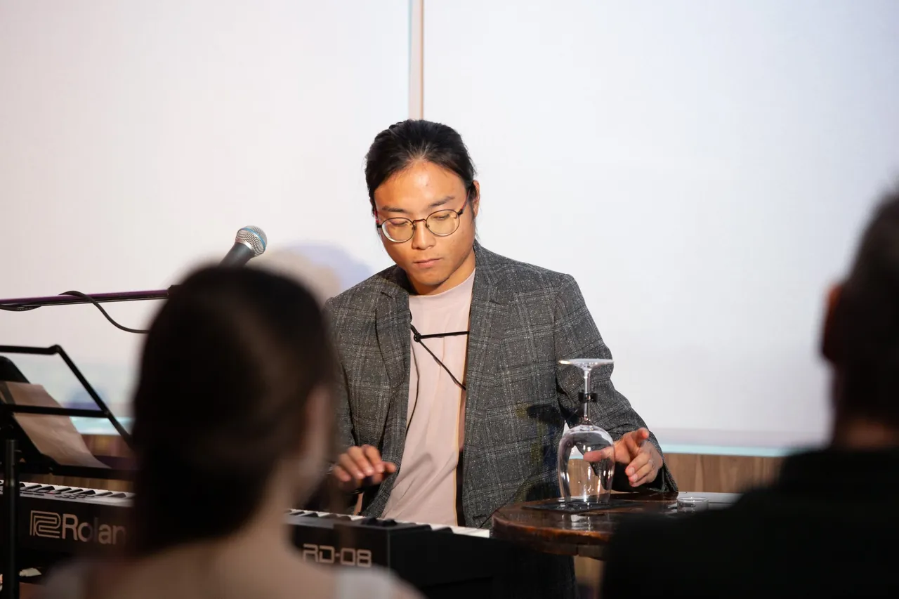 Aaron reaching toward an upturned wine glass on a table next to a Roland keyboard.